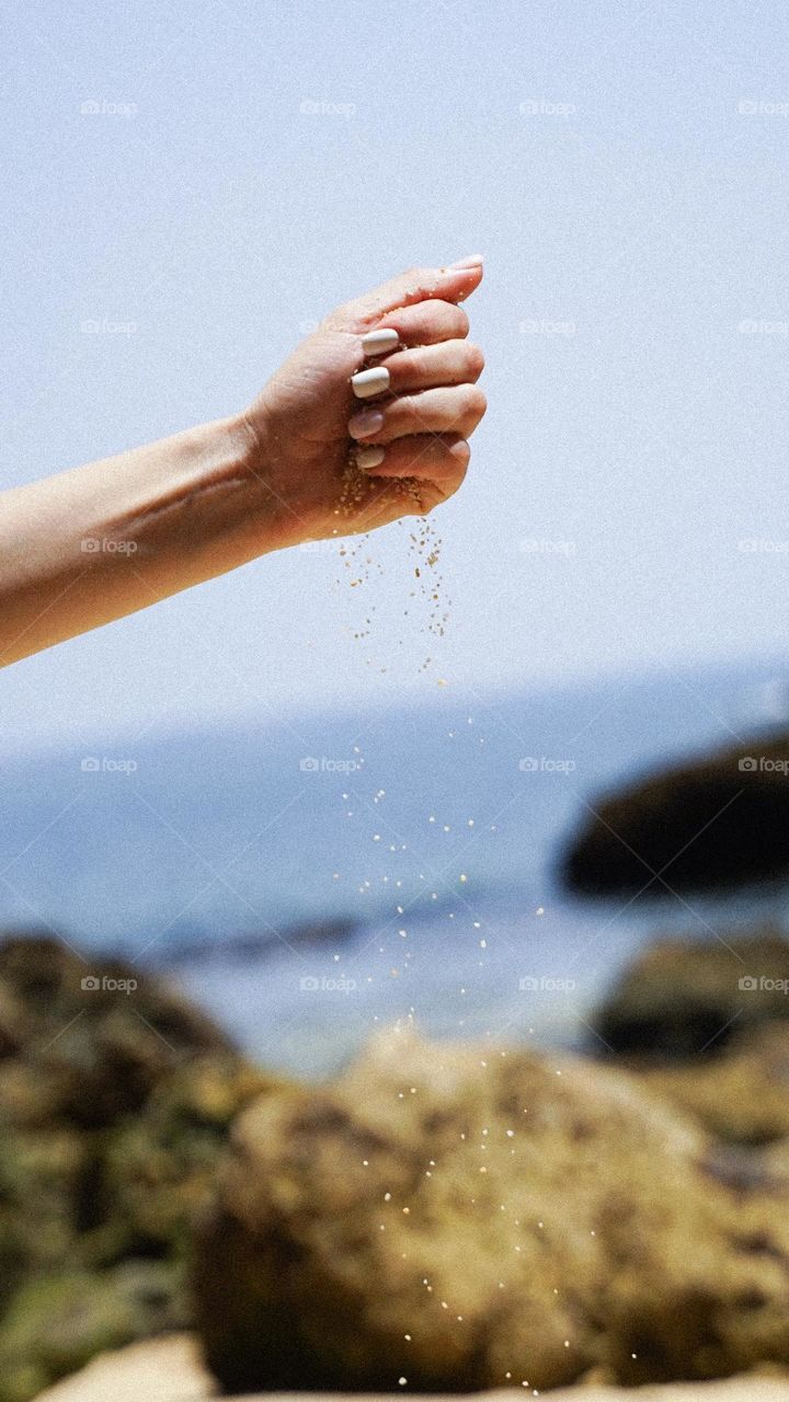 Woman manicure. Female hand pouring sand on the sea beach. Beautiful nails. Copy space