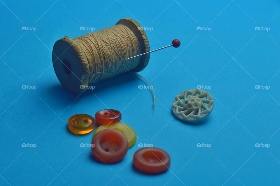 several colored buttons and an old wooden spool of thread on a blue background.