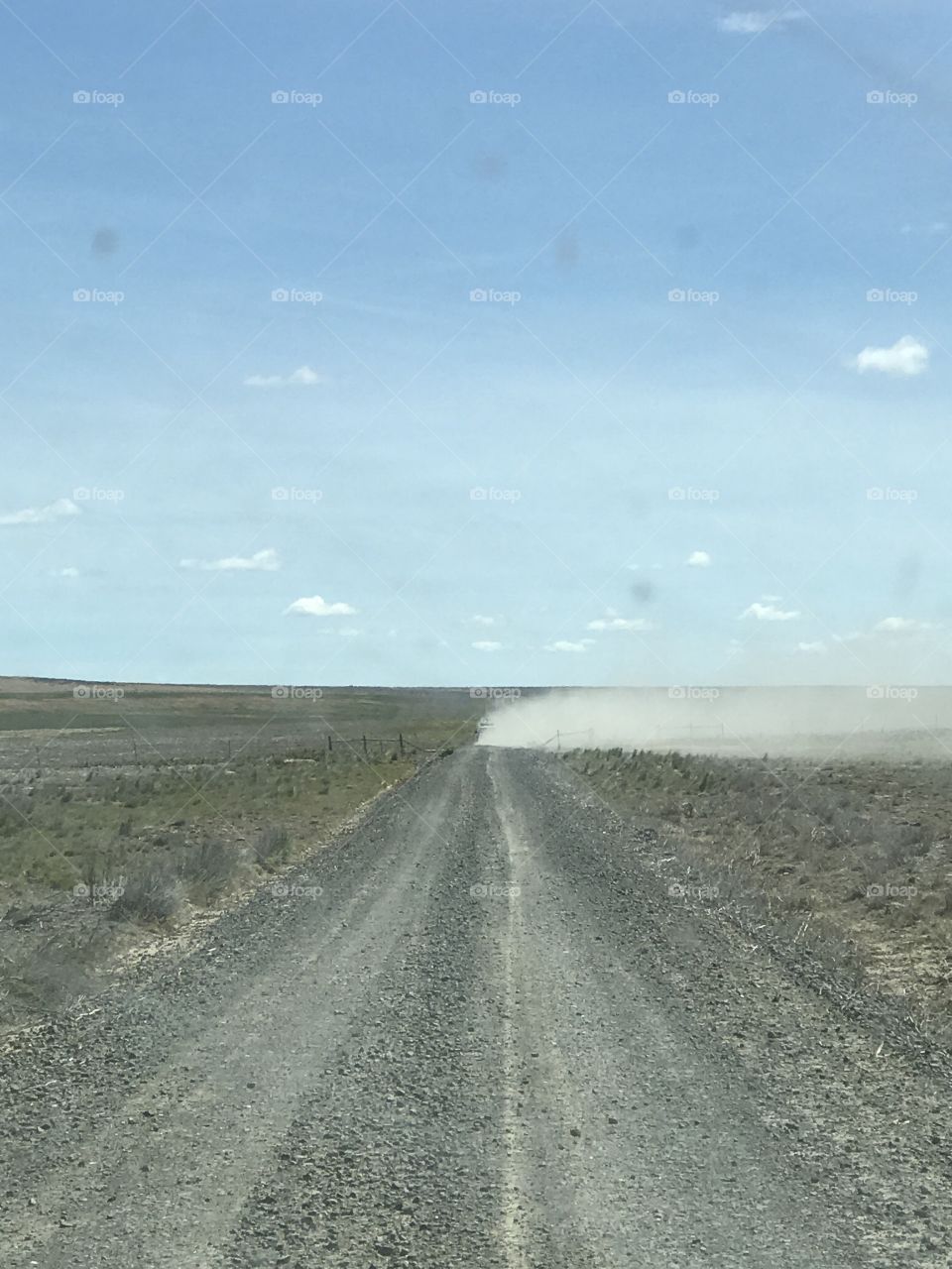 Driving down country dirt road, alone ,isolated dust in the air. Wide open land for as far as you can see.