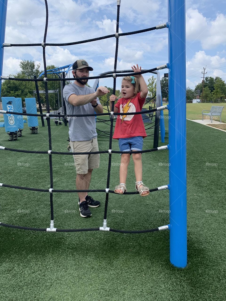 A dad helping his daughter climb at a park 