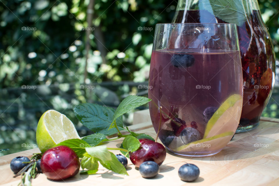 Healthy antioxidant rich flavored water in pitcher with glass on patio table outdoors in summer with dark red cherry, blueberry, lime slice and fresh mint ingredients for summer refreshing drink or beautiful garden party drinks 