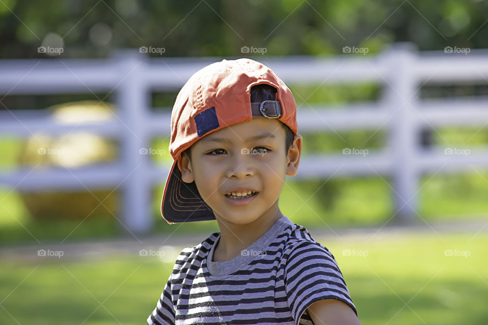 Portrait of Asian boy wearing a hat and smiled happily on the lawn.