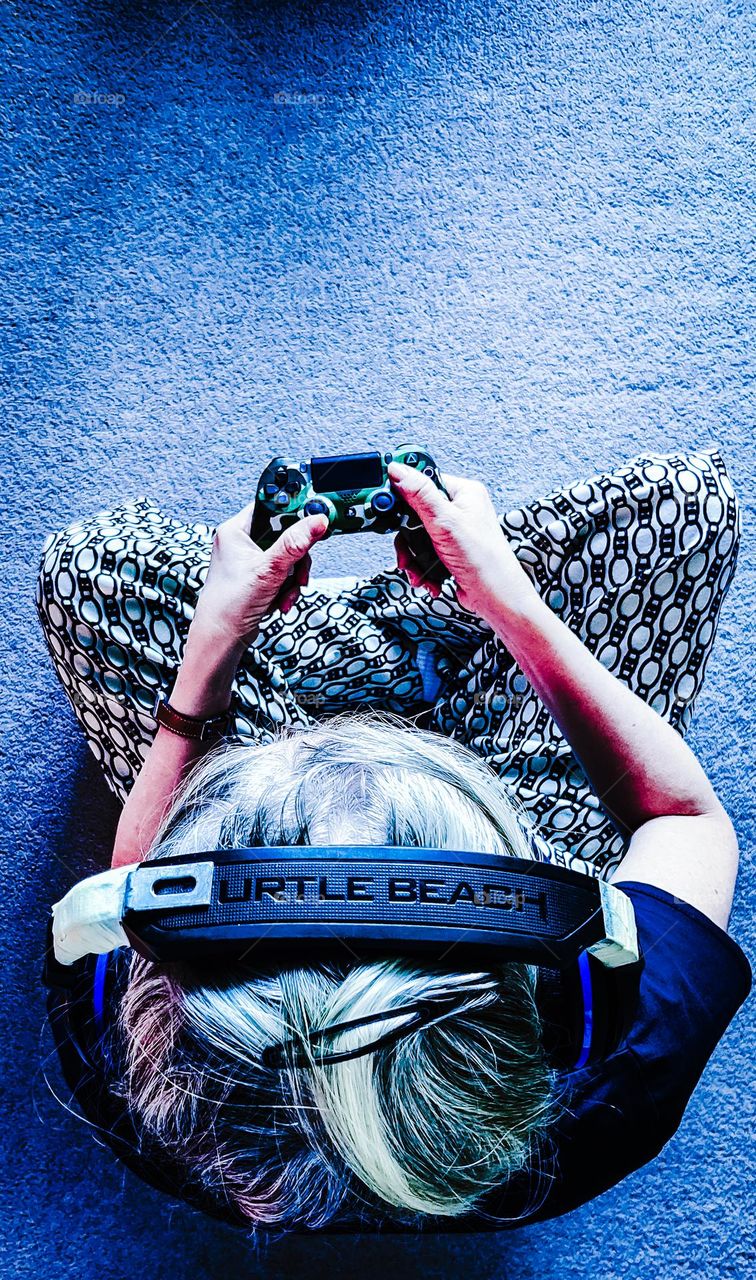 Woman playing a PS4 video game cross legged with old headphones held together with a piece of metal and masking tape.