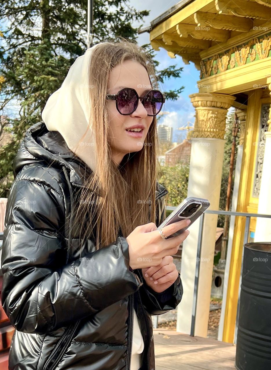 Girl in a hood and sunglasses holding a phone