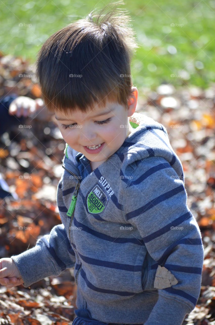 Toddler boy smiling and playing in a pile of fall leaves