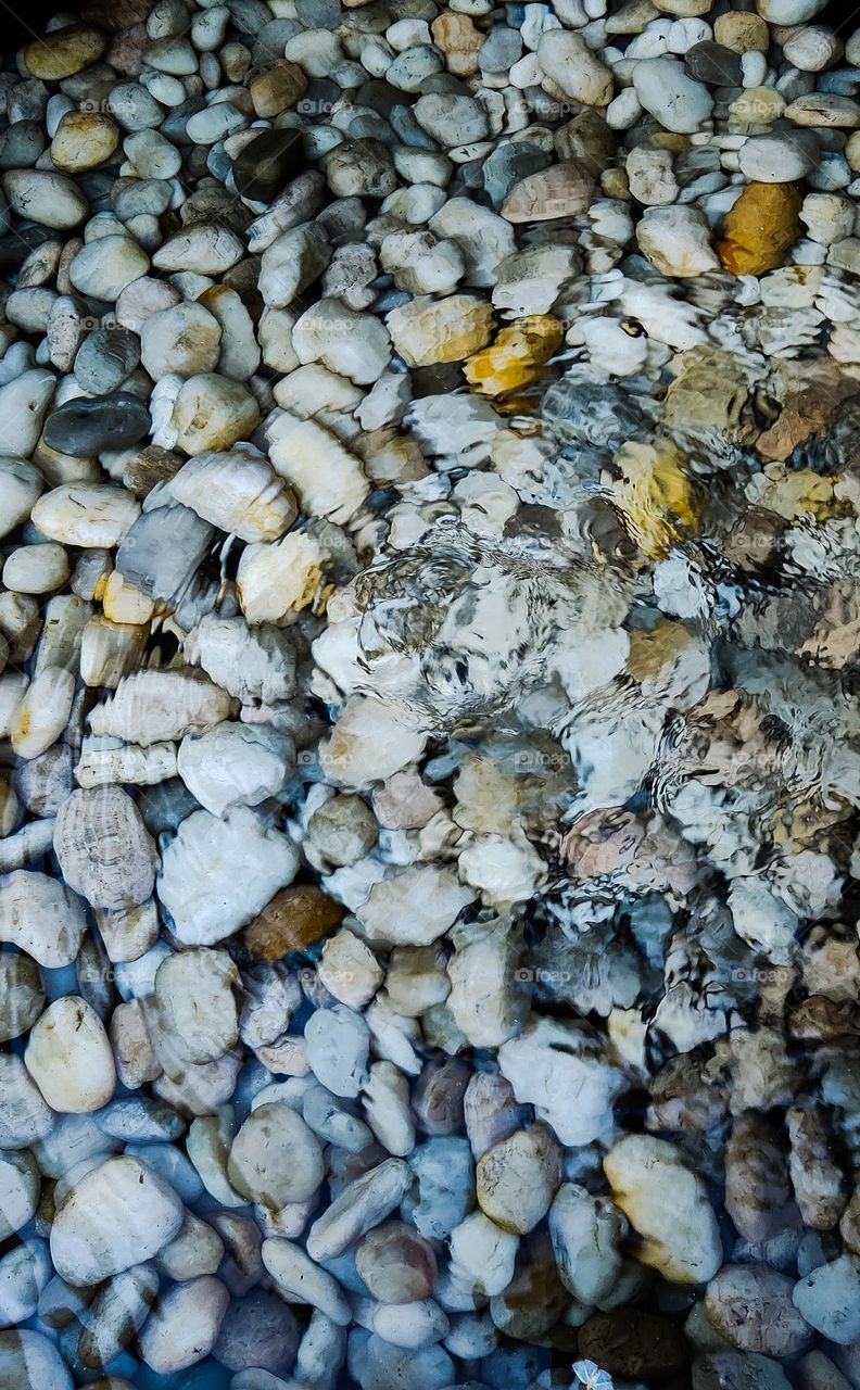 Whirlpool of water on top of colorful rocks and pebbles.