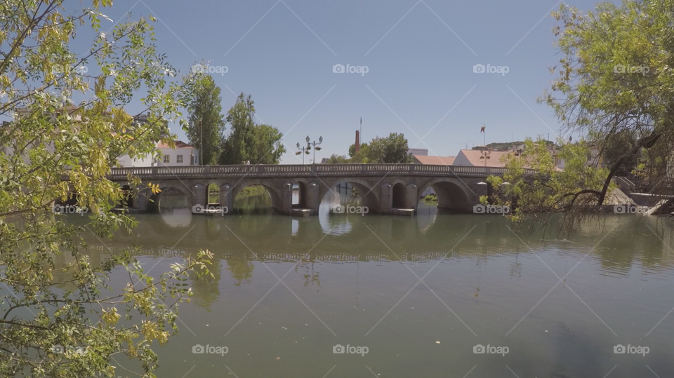 , in Tomar, Portugal Old sleek polished little bridge made of stone over a green river with a clear blu sky