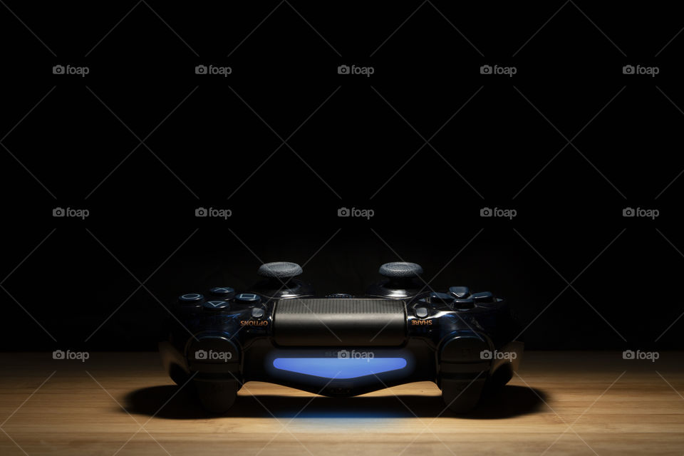 A close up portrait of a turned on PlayStation 4 controller with a blue light as its indicator emerging from the darkness.