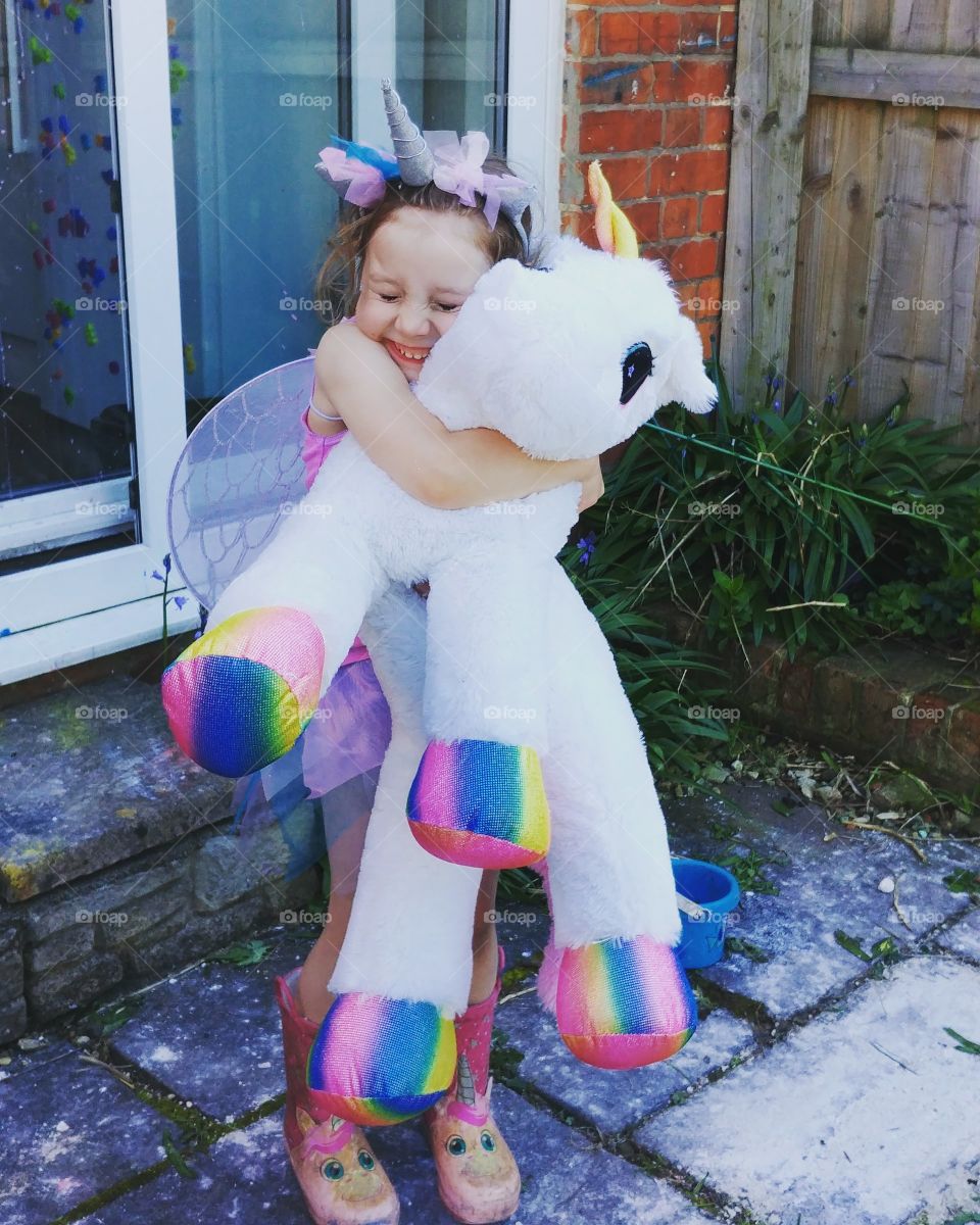 little girl hugging toy unicorn dressed as fairy