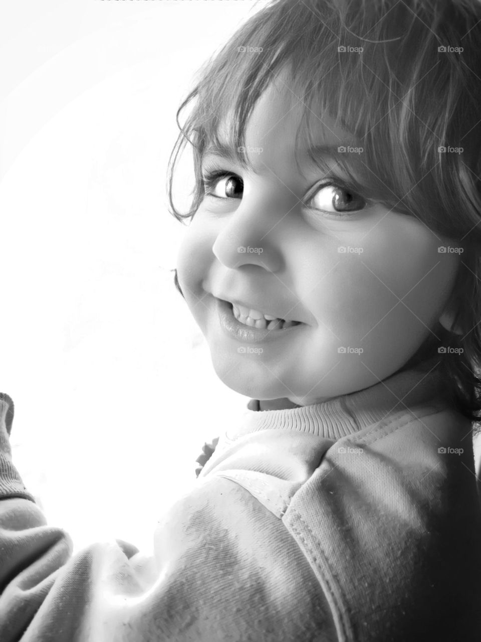 My niece is standing in front of the window and looking at me with simple smile and eyes full of love , black and white background