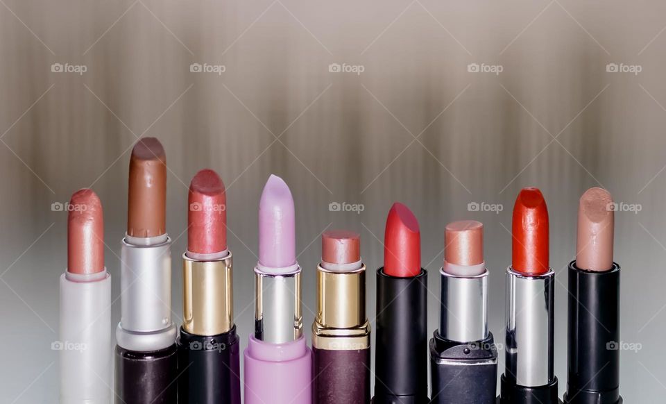 A row of lipsticks of various colours and of varying degrees of wear, with unusual shadow causes by LED light