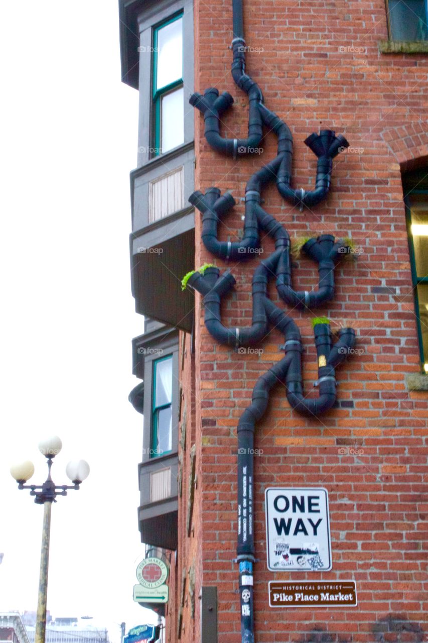 Cool urban public art - creative drain spout design on a brick building next to a one way street sign