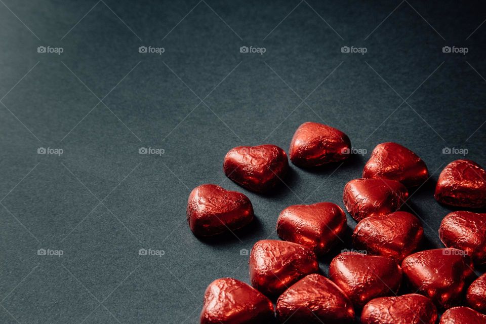 A red foil-stamped chocolate heart is placed in the bottom left corner of the black background.