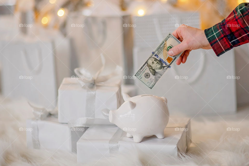 piggy bank with 100 dollars banknote in festive New Year atmosphere of scenery.  Magical bokeh with Christmas tree and bright lights.