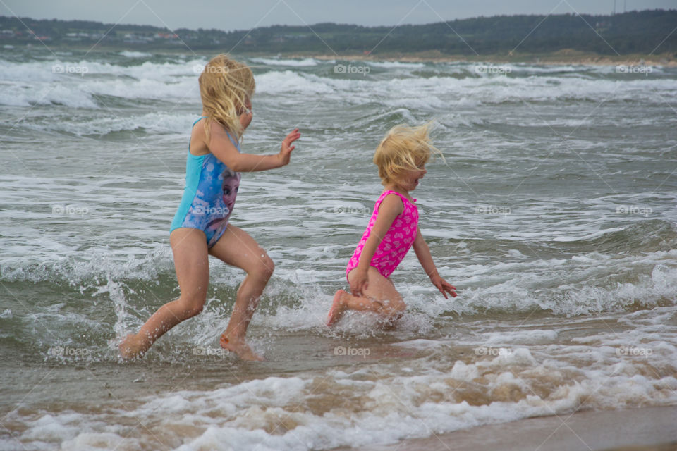 Twi sisters playing at the beach of Tylösand outside Halmstad in Sweden. It's about to get stormy weather but the girls is having fun swimming and playing in the water.