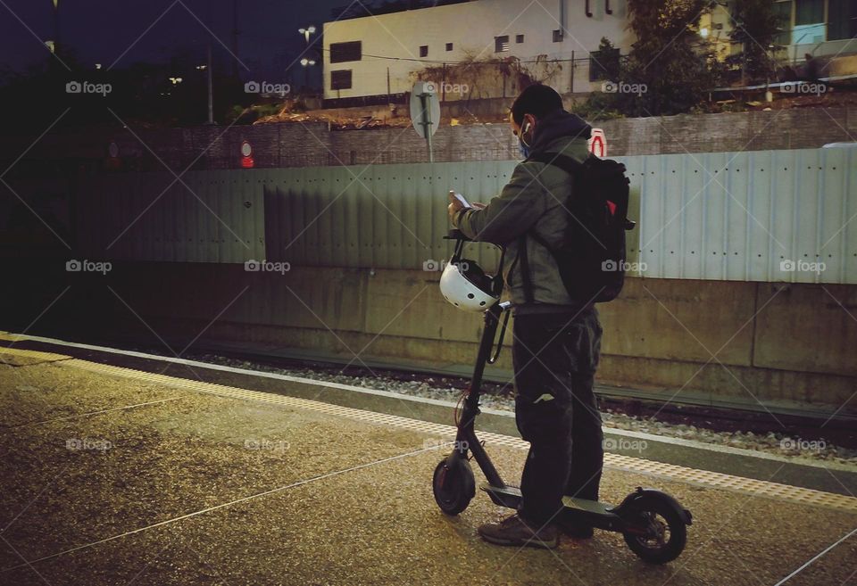 A young Israeli man with a scooter waiting for the evening train
