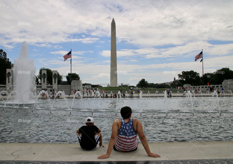 Two boys in front of fountain looking at Washington  monument 