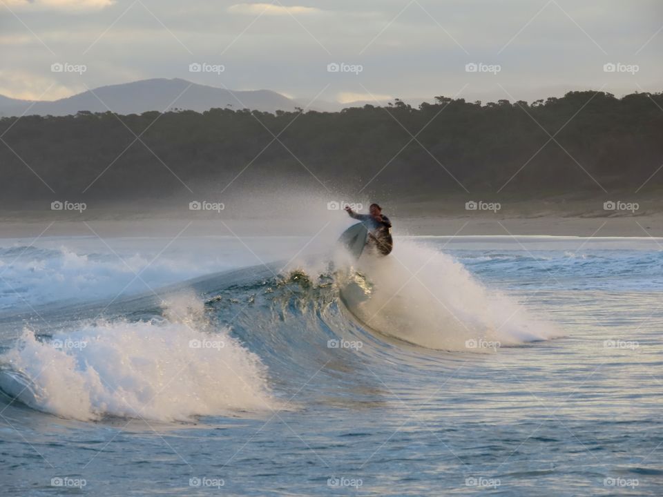 Summer time: surfer doing tricks up and down the wave and sunset on the Australian coastline.