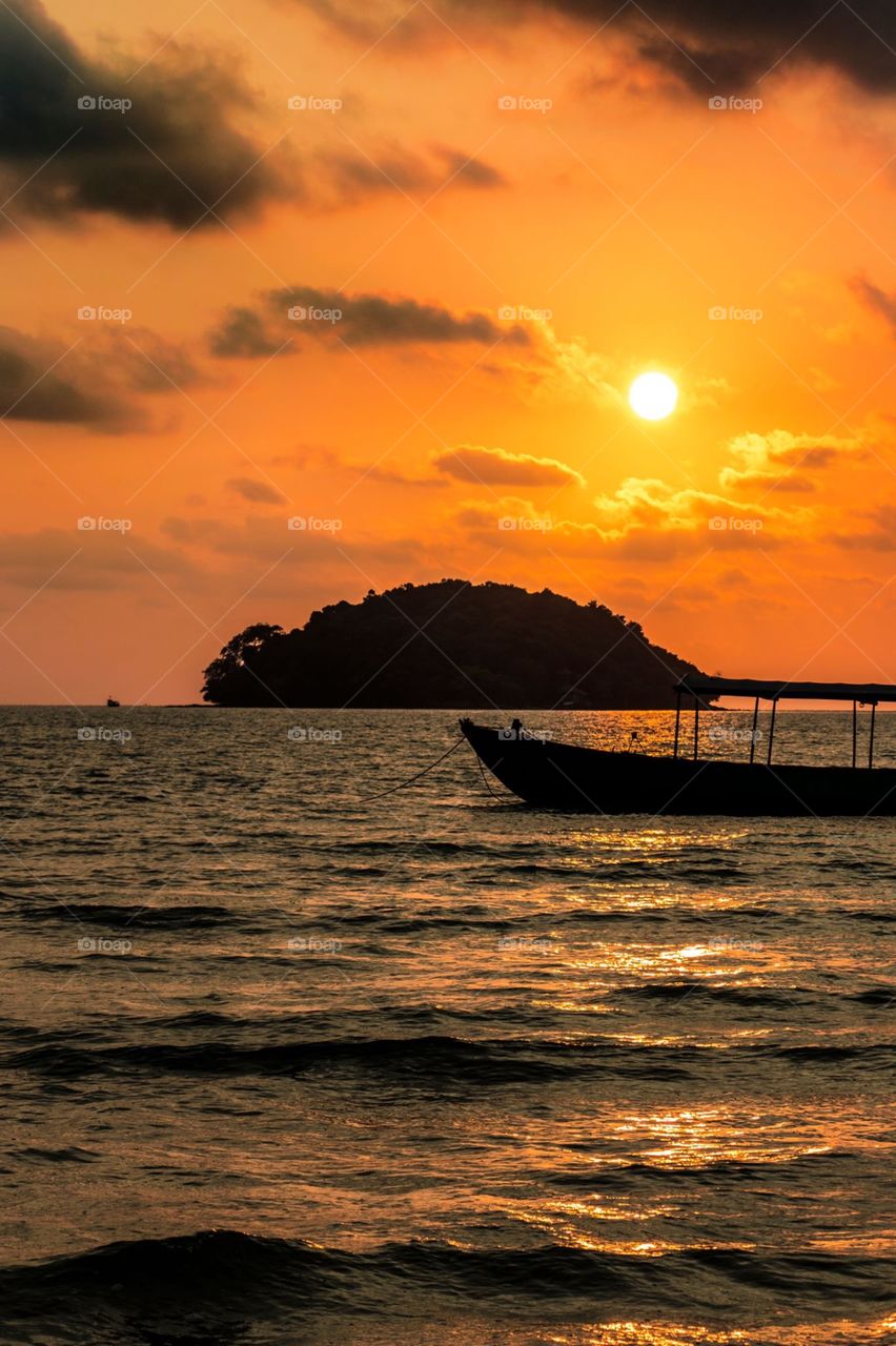 Sunset over Otres Beach in Cambodia, with silhouette of a small island and a long boat in the foreground.