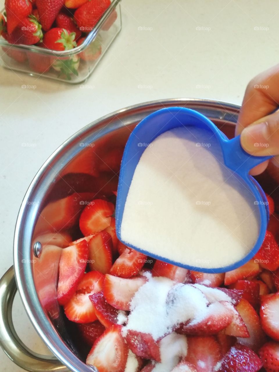 Measuring sugar for strawberry preserves with bowl of strawberries in background
