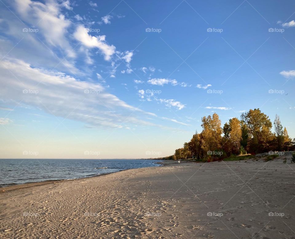 Liquid Fresh water Lake Eerie on Cedar Point shoreline and sandy, rocky beach with blue sky divided by a white cloud with trees in the distance 