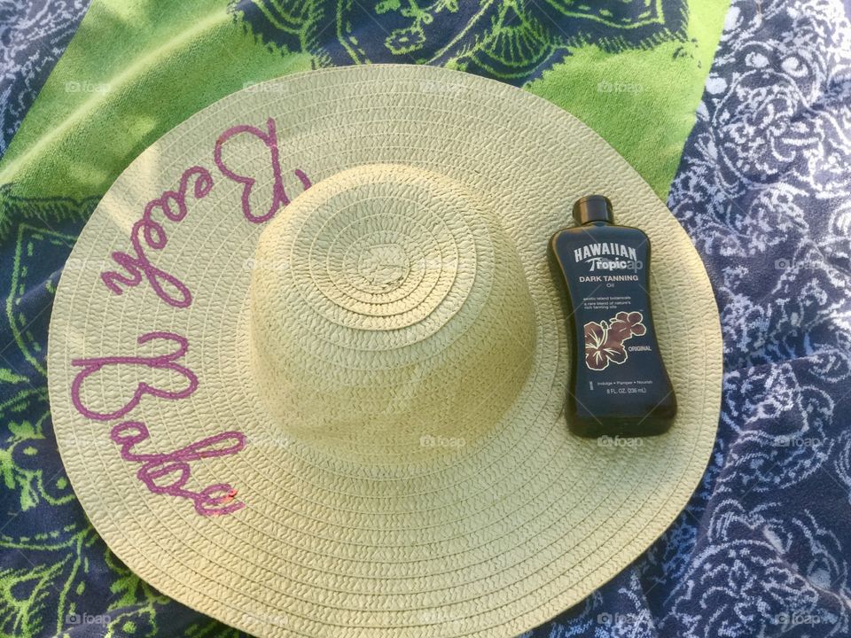 Straw hat and Hawaiian tropic tan lotion on display on a beach towel outside on a summers day. Flat lay 