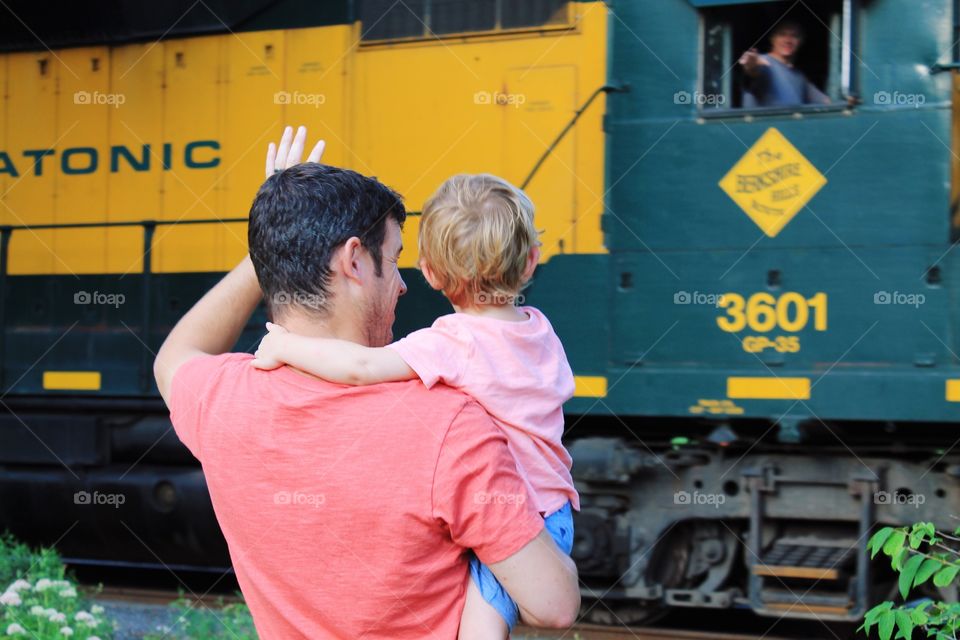Rear view of a father carrying his son standing in front of train
