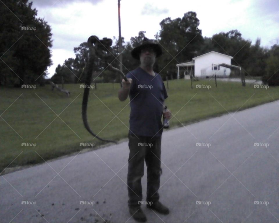 Snake in the road.  Man found a chicken snake beside the road and had to play with it