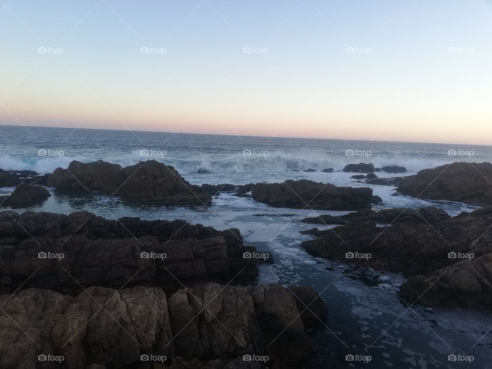 Shows the waves of the ocean and the ending of a sunset with rocks and a amazing landscape.