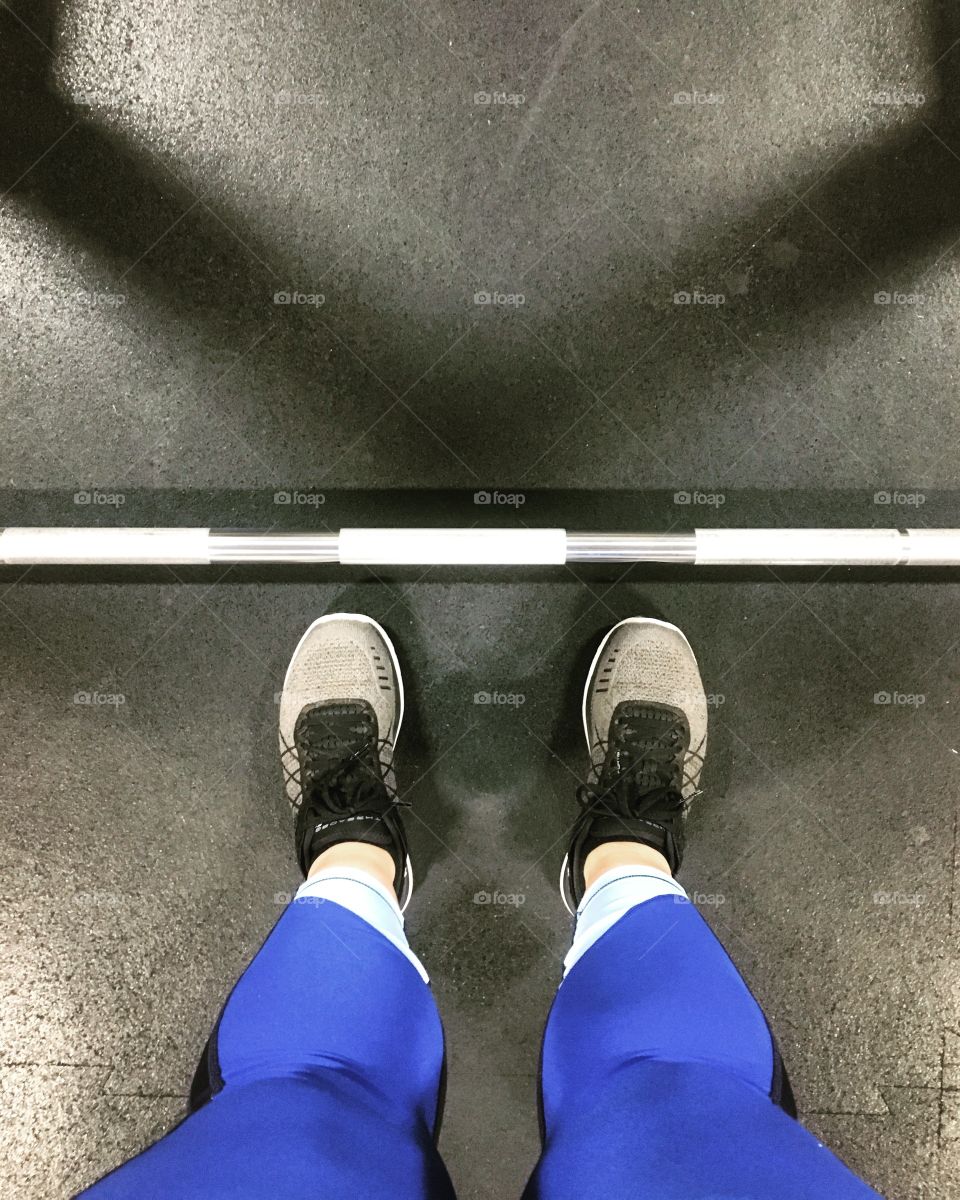 Downward view of woman’s feet and a barbell bar in a gym
