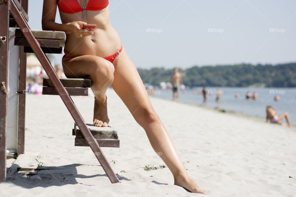 Low section of a woman in bikini using cell phone