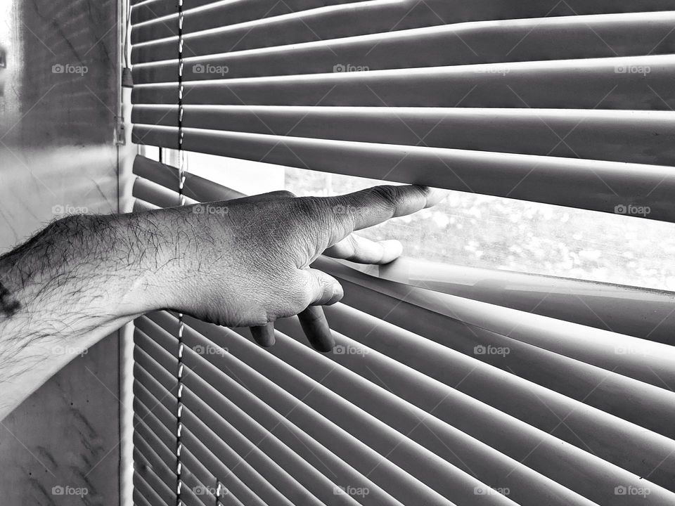 man's hand pushes back the window blinds on the window