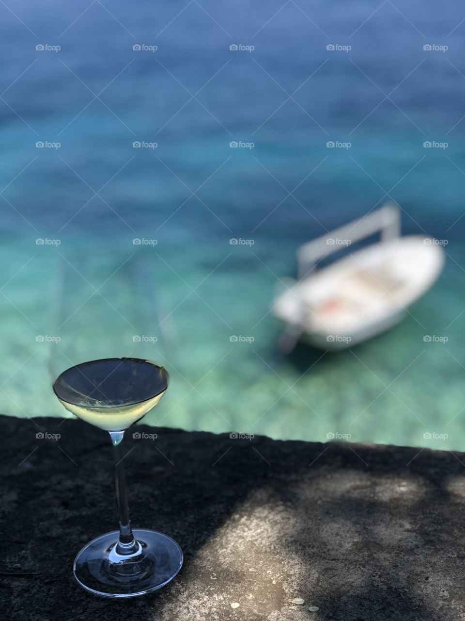 Enjoying a glass of white wine over looking the Beautiful clear green blue Adriatic Sea in Korcula Croatia Where a boat is floating in the background