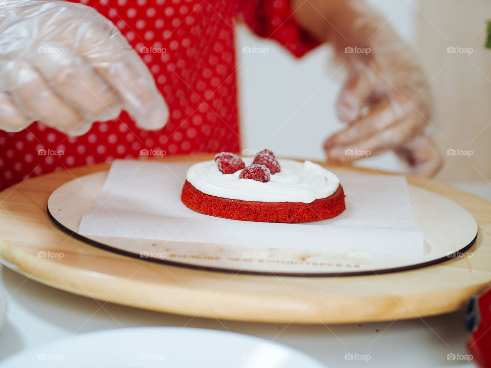 Woman confectioner in red dress making red velvet cake with berries