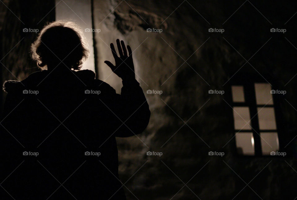 Silhouette of a woman with a hand up, light behind her head and a window on the house wall