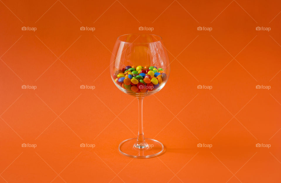 Sweet colorful candies in a glass on the orange colored background