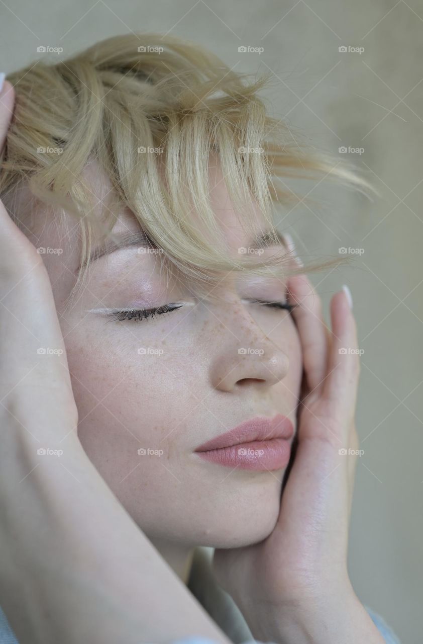 Portrait of a cute girl with blond hair with a beautiful look with her hands near her head