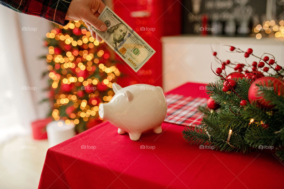 piggy bank with 100 dollars banknote in festive New Year atmosphere of scenery. Magical bokeh with Christmas tree and bright lights.