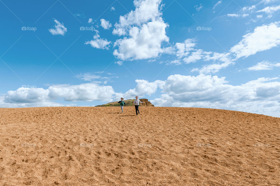 Two children, boy and girl running downhill on the sand dunes  on Jurassic Coast in Dorset. UK.
