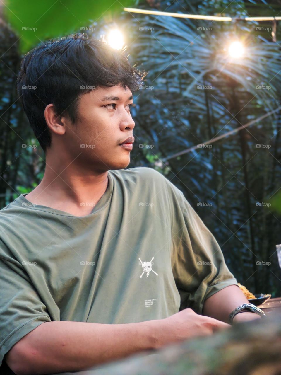 Young man looking away while standing against trees