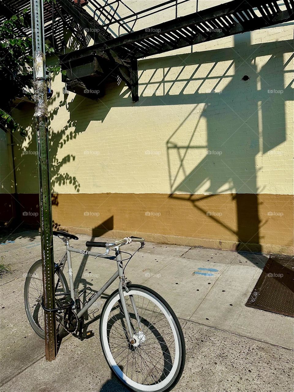 Dramatic shadows are cast onto this facade on “Jefferson St” off “Broadway” in “Bushwick”, Bklyn by the intricate multifaceted structures of the “M” train overpass at the “Myrtle Ave” station in the late afternoon sun. 2024. Hypnotic Productions