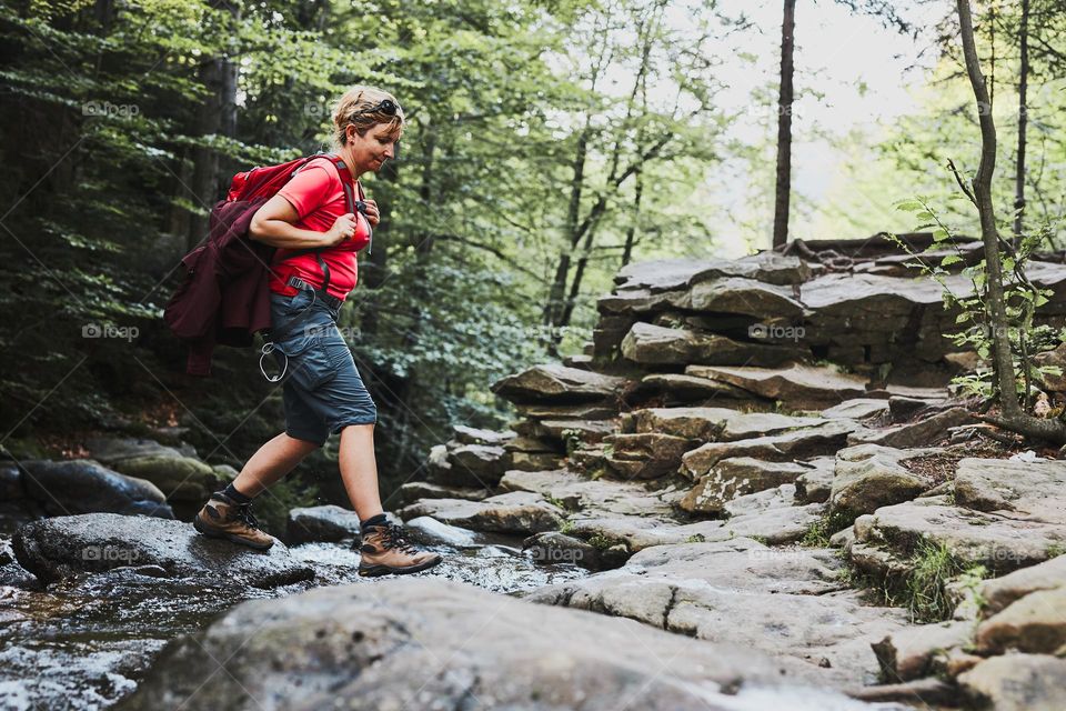 Woman with backpack hiking in mountains, spending summer vacation close to nature. Woman crossing the mountain stream