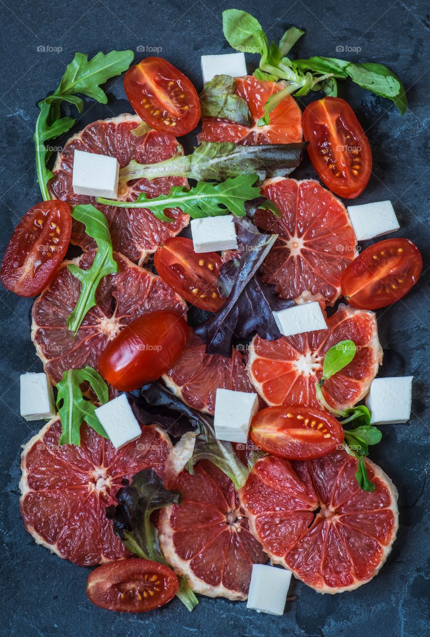 Summer salad of red grapefruit, arugula, lamb's lettuce, red lettuce, mini Roma tomatoes and feta cheese on a slate.