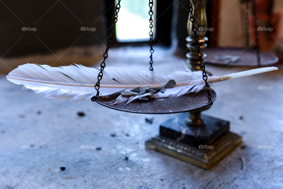 Balance scale with a feather and slivers of stone in front of the natural light from a window