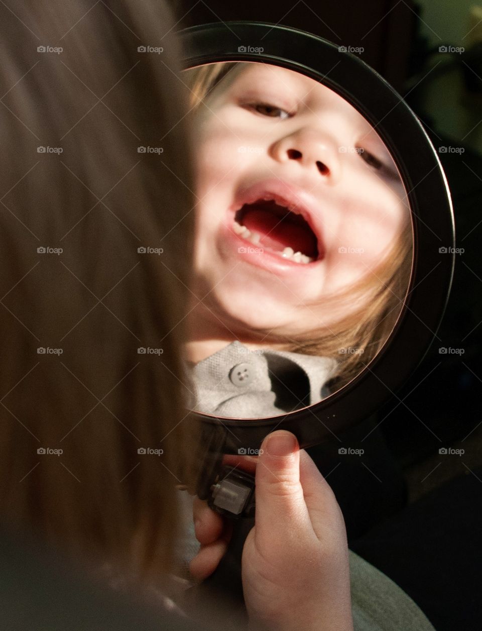 Little girl looking at her missing front teeth in a hand held mirror