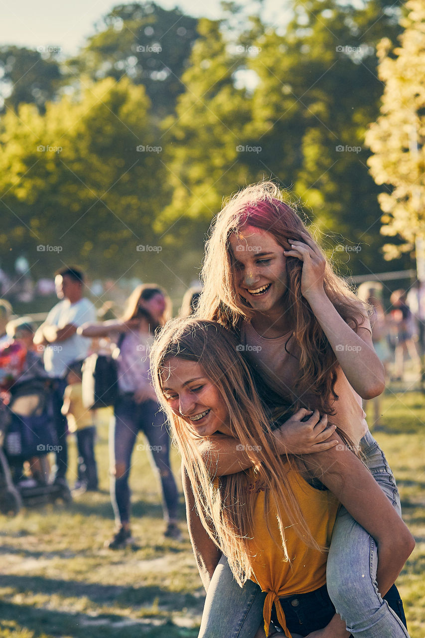 Portrait of happy smiling young girls with colorful paints on faces and clothes. Two friends spending time on holi color festival. Real people, authentic situations