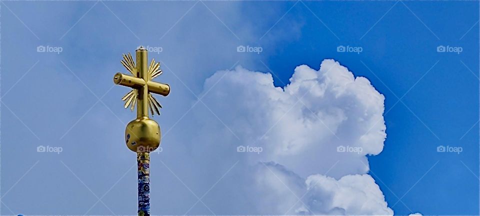 A golden globe, a cross above it and rays extending toward the sun against a blue sky with cumulus clouds marks the highest point of the “Zugspitze” summit at 2962 m. It is the tallest mountain in the German “Alps”. 2024. Hypnotic Productions