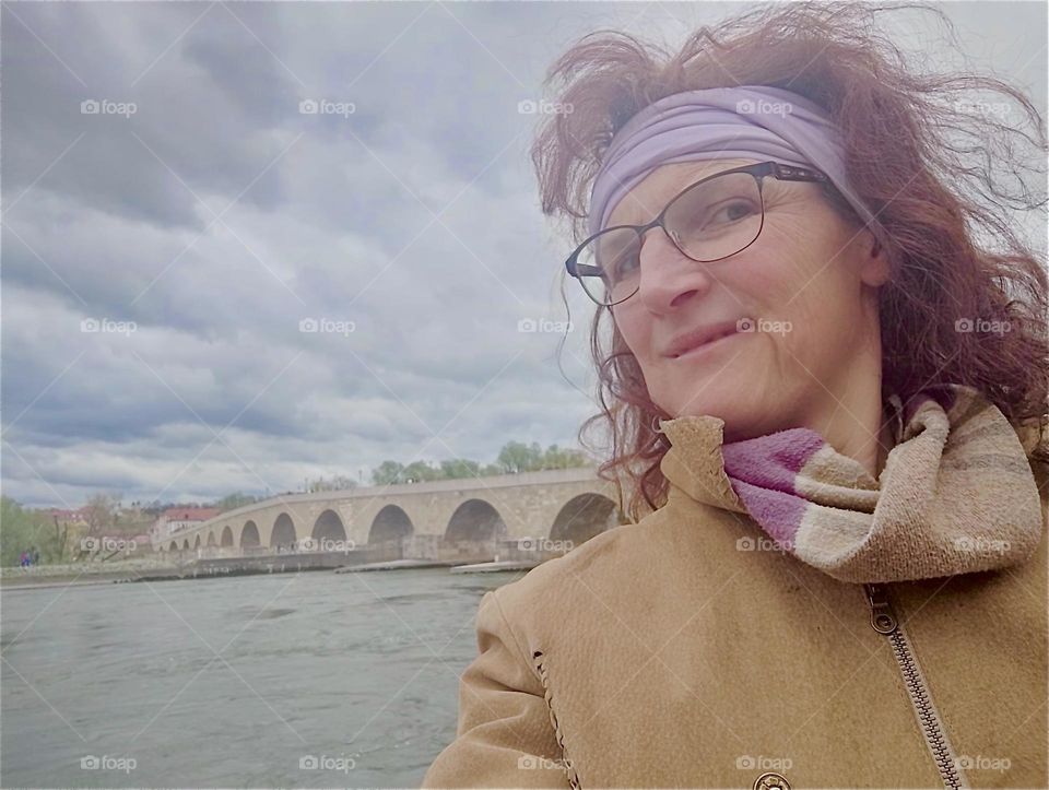 This young lady is standing at the banks of the river “Danube” by the “Steinerne Brücke”, the “Stone Bridge” that was built over a 1000 years ago in “Regensburg”, “Bavaria”, Germany. 2024. Hypnotic Productions